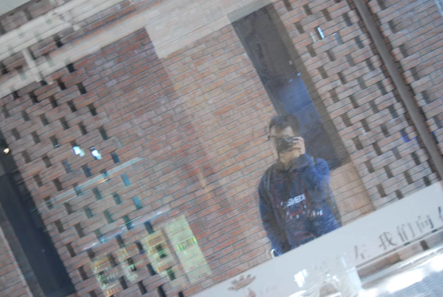Kyle's reflection in the window of a brick building, camera raised